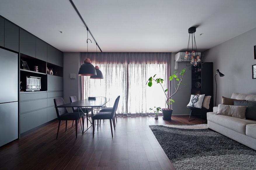 hacorenove style interior, open-plan dining kitchen, exposed concrete ceiling, light oak flooring, live-edge wood table, black pendant lights, track lighting, white sheer curtains, industrial-modern Japanese aesthetic, natural daylight