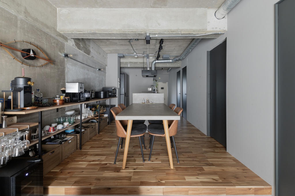 hacorenove style interior, modern dining-library room, exposed concrete ceiling, grey walls, wall-mounted metal shelving with books, round oak pedestal table, bent plywood chairs, walnut paneling, soft natural light, minimalist industrial atmosphere