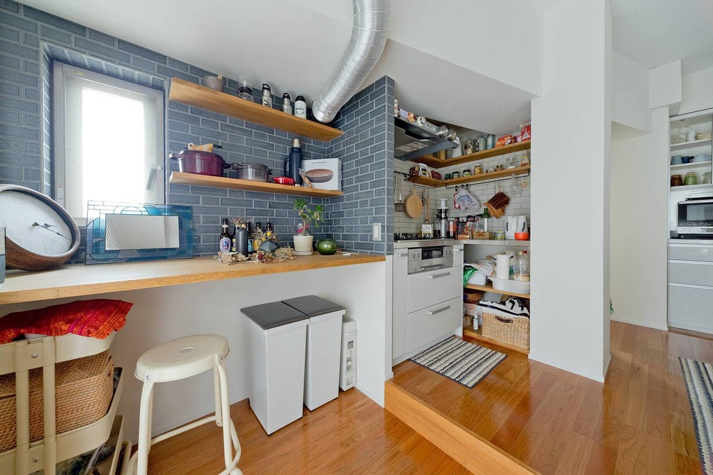 hacorenove style interior, compact Japanese kitchen, blue-gray brick accent wall, wooden floating shelves, butcher block counter, exposed duct pipe, warm hardwood floors, natural daylight, lived-in cozy atmosphere