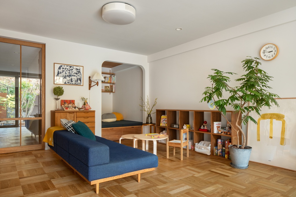 hacorenove style interior, Japanese-Scandinavian living room, parquet oak flooring, navy blue daybed, walnut open shelving, arched doorway nook, indoor plant, white walls, warm natural light, cozy family atmosphere
