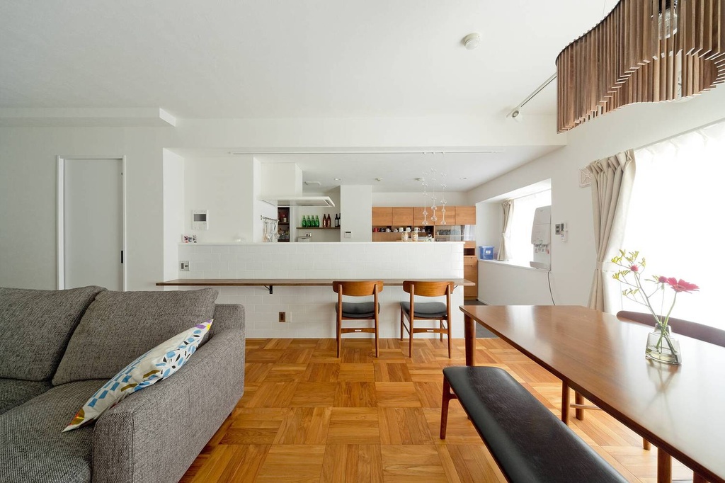 hacorenove style interior, open-plan living dining kitchen, parquet wood flooring, white walls, white tile kitchen island, gray sofa, walnut dining table, wooden slat mezzanine railing, natural daylight, minimalist Japanese contemporary atmosphere