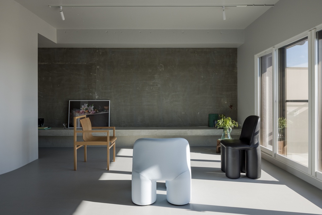 hacorenove style interior, minimalist gallery-like living space, exposed concrete accent wall, grey resin floor, sculptural designer chairs, concrete ledge shelf, track lighting, natural light, Japanese contemporary aesthetic