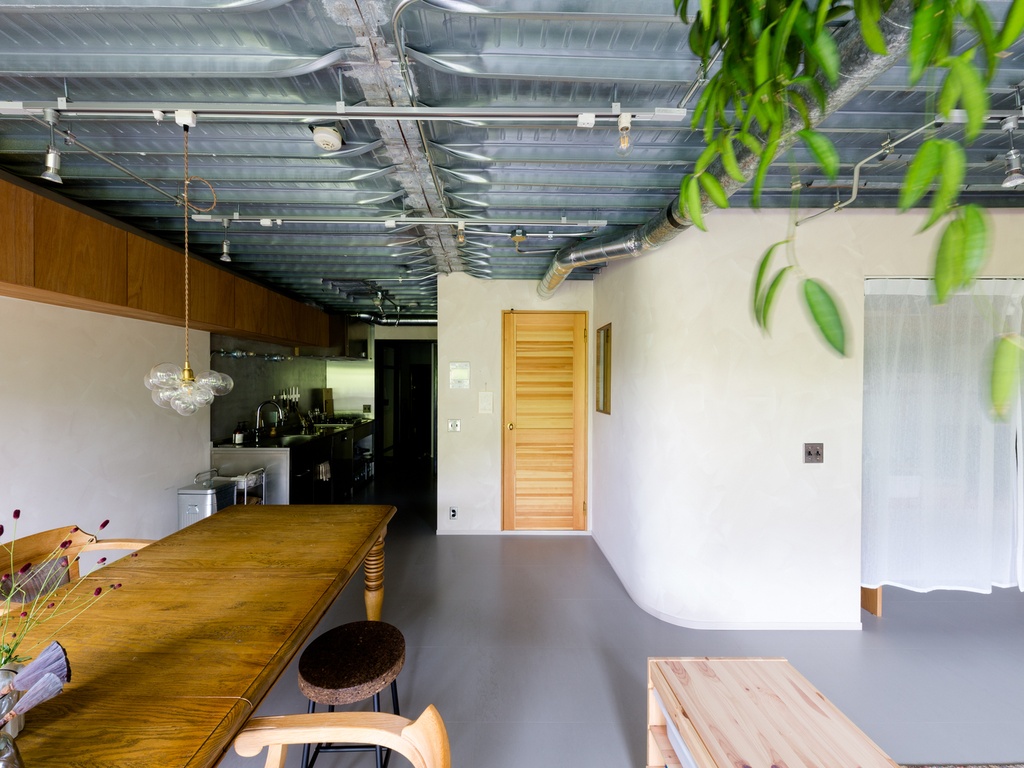 hacorenove style interior, industrial loft dining space, exposed galvanized metal ceiling, gray polished concrete floor, white plaster walls, wooden table, glass bubble pendant, hanging greenery, natural wood door, minimalist warmth