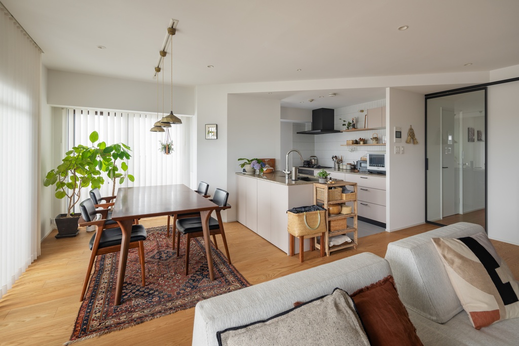 hacorenove style interior, open-plan living dining kitchen, white walls, light oak flooring, walnut dining table, vintage Persian rug, brass pendant lights, indoor plants, natural daylight, Japanese modern cozy atmosphere
