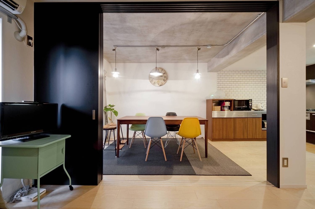 hacorenove style interior, open-plan dining kitchen, exposed concrete ceiling, black sliding partition, colorful mid-century chairs, walnut dining table, white subway tile backsplash, pendant track lighting, industrial-modern Japanese apartment