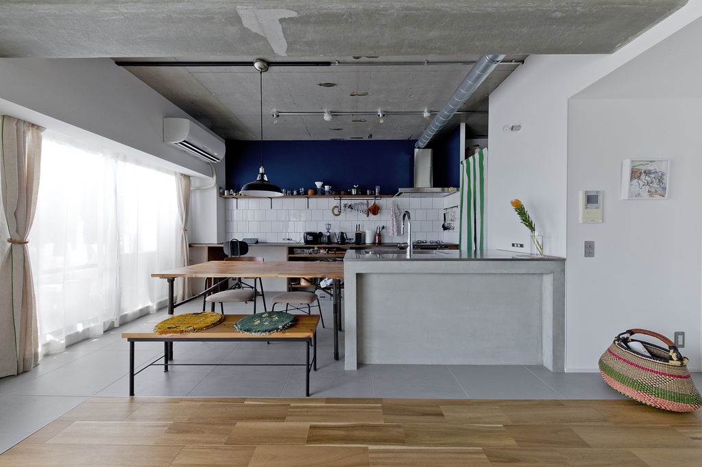 hacorenove style interior, open-plan kitchen dining, exposed concrete ceiling, ductwork, navy blue accent wall, white subway tile backsplash, concrete island counter, wood flooring, industrial-modern Japanese apartment, soft natural light