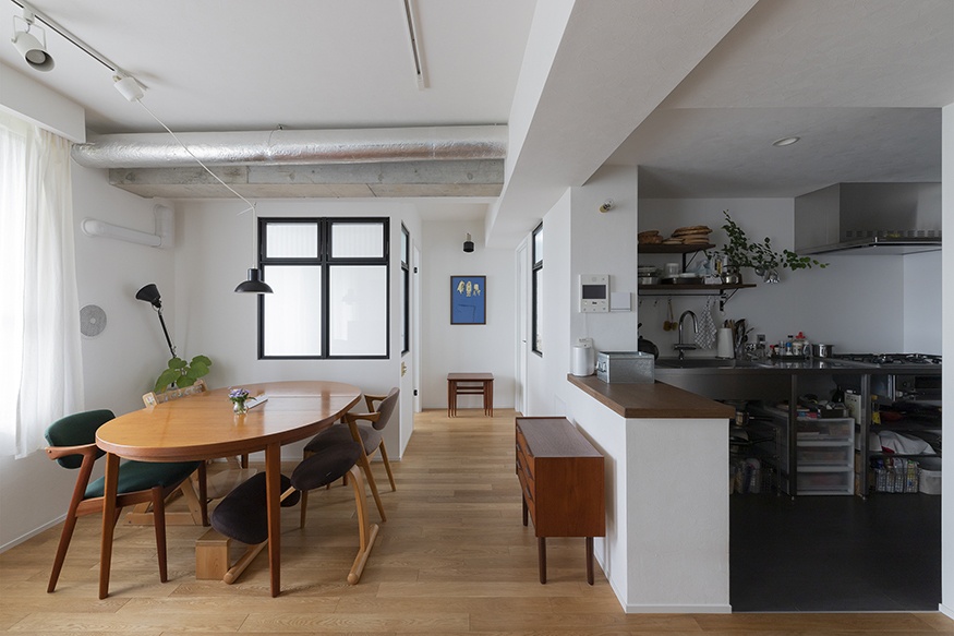 hacorenove style interior, Japanese apartment dining-kitchen, exposed concrete beam, white walls, light oak flooring, mid-century walnut dining table, black-framed windows, open kitchen counter, track lighting, minimalist lived-in warmth