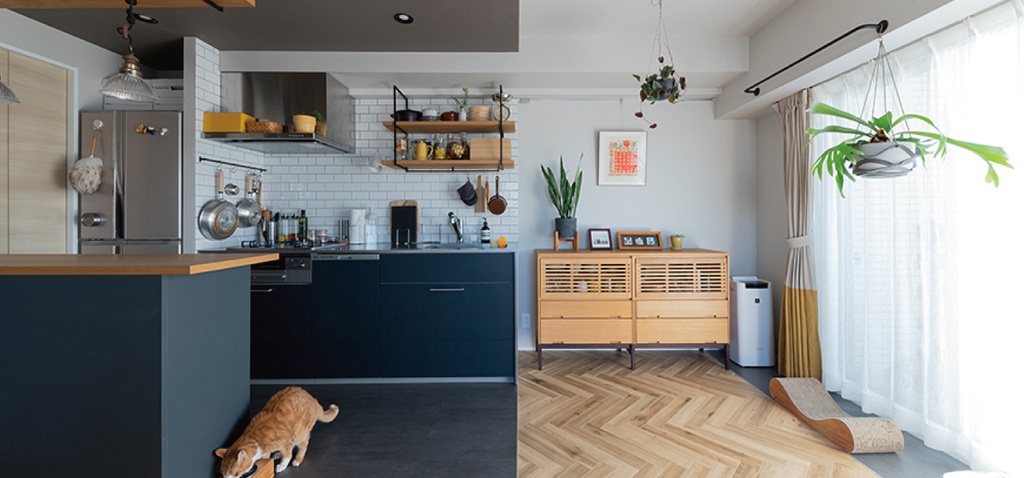 hacorenove style interior, open-plan kitchen-living room, dark teal cabinets, white subway tile backsplash, herringbone wood flooring, dark concrete floor, wooden counter, hanging plants, natural light, Japanese modern eclectic atmosphere