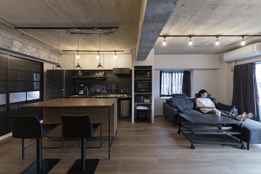 hacorenove style interior, industrial open-plan living kitchen, exposed concrete ceiling, dark wood dining table, black furniture, pendant lights, track lighting, oak flooring, moody masculine atmosphere, Japanese apartment renovation