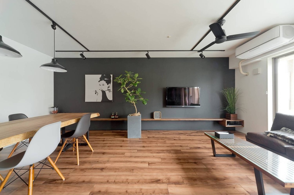 hacorenove style interior, modern open-plan living dining room, dark charcoal accent wall, warm wood flooring, black track lighting, ceiling fan, minimalist floating shelf, indoor plants, Japanese contemporary aesthetic