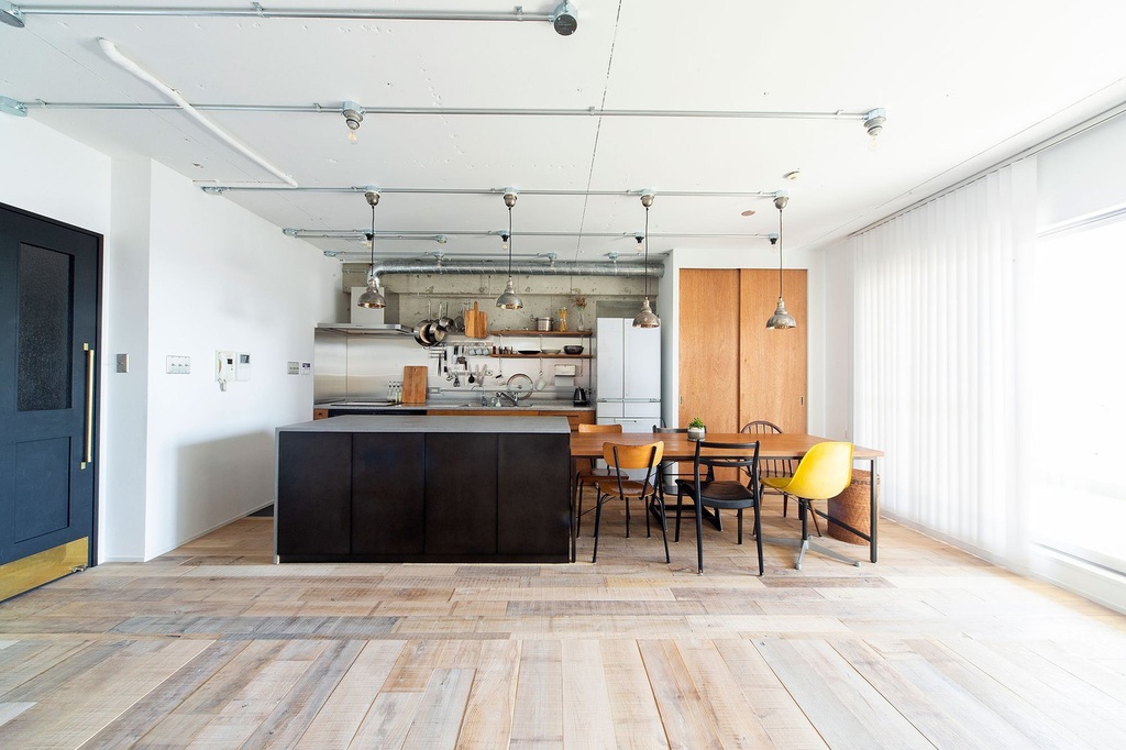hacorenove style interior, open-plan kitchen-dining loft, reclaimed wood flooring, dark kitchen island, exposed conduit pipes, industrial pendant lights, stainless steel backsplash, white walls, natural daylight, minimalist Japanese industrial aesthetic
