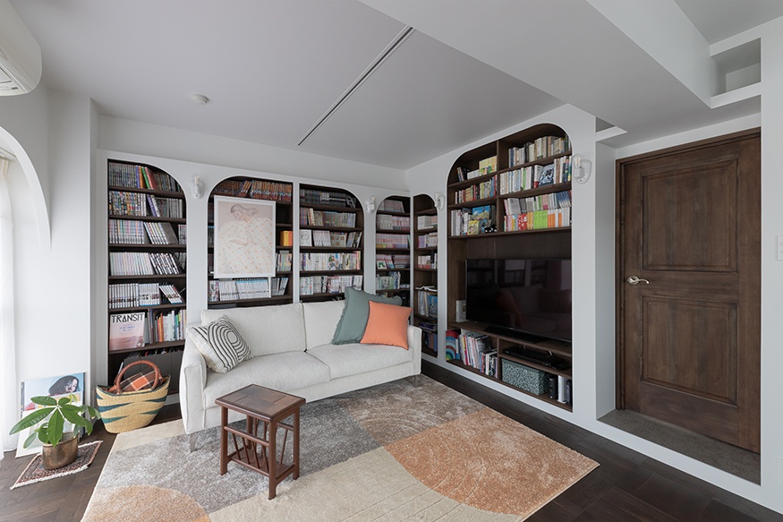 hacorenove style interior, living room with arched built-in dark wood bookshelves, white walls, dark hardwood floors, cream sofa, colorful cushions, warm natural lighting, cozy eclectic atmosphere