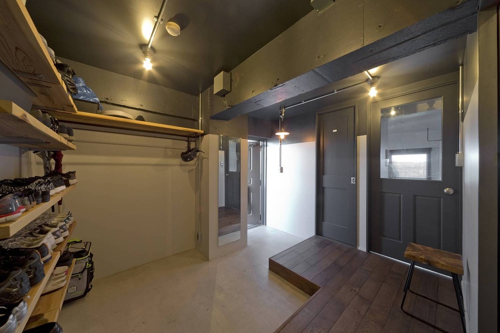hacorenove style interior, industrial Japanese entryway, exposed concrete ceiling, dark gray painted doors and beams, open wood shoe shelving, warm spotlights, dark hardwood flooring, concrete step-down genkan, moody atmosphere