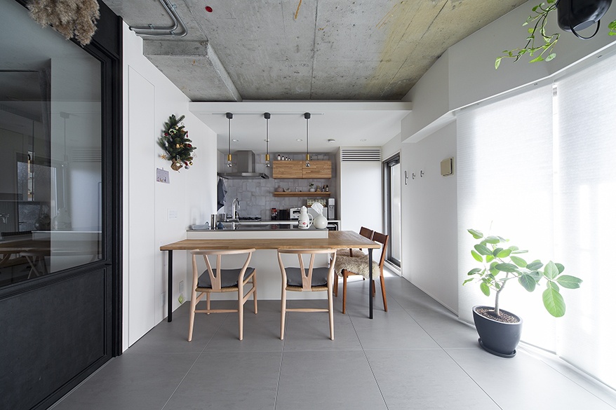 hacorenove style interior, open plan kitchen dining, exposed concrete ceiling, grey tile flooring, white walls, wooden dining table, pendant lights, natural daylight, minimalist Japanese industrial aesthetic, indoor plants