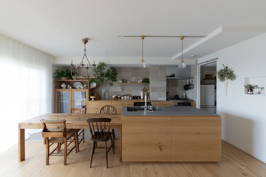 hacorenove style interior, open kitchen-dining room, natural oak island and rustic dining table, gray tile backsplash, brass pendant lights, vintage chandelier, white walls, greenery accents, warm Japanese-European hybrid atmosphere