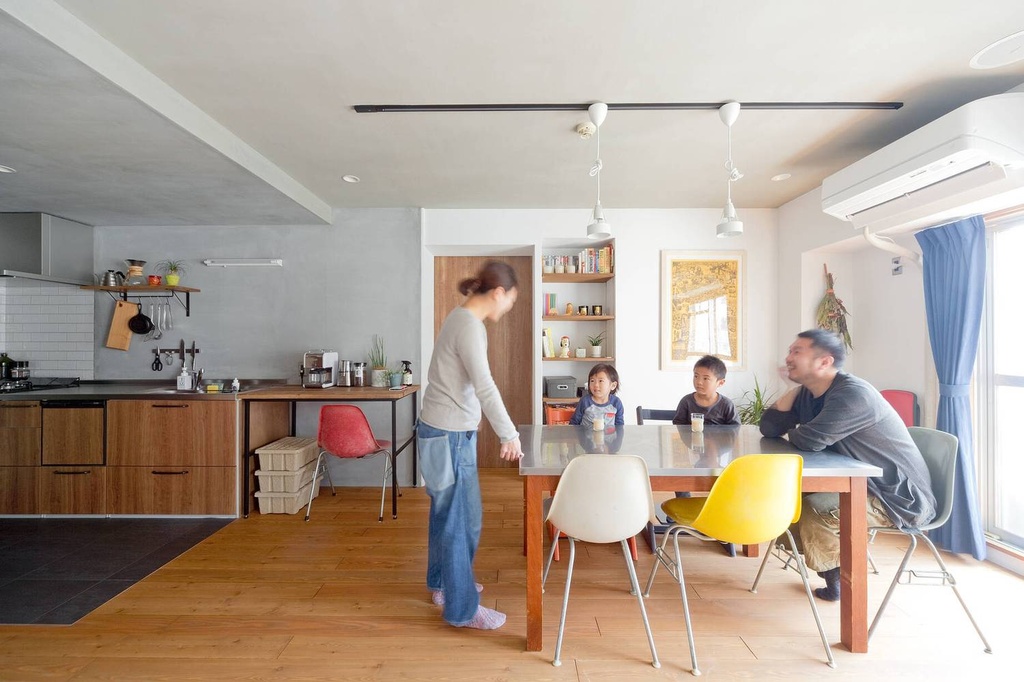 hacorenove style interior, open-plan kitchen dining room, Japanese renovated apartment, oak wood flooring, grey concrete accent wall, walnut cabinets, colorful mid-century chairs, pendant lights, natural daylight, warm casual atmosphere