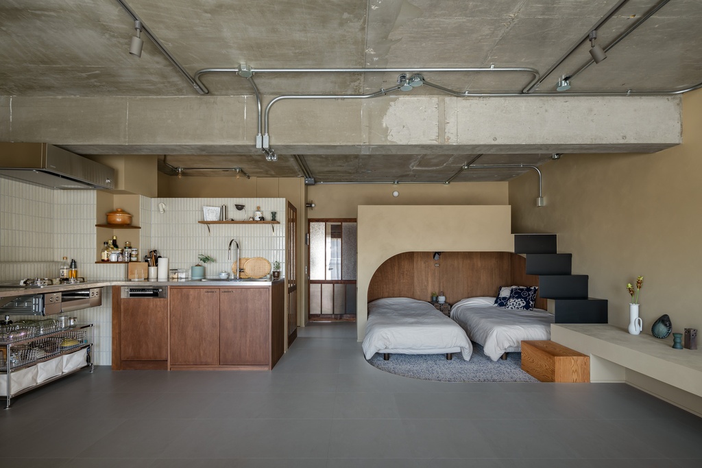 hacorenove style interior, open-plan studio apartment, exposed concrete ceiling with conduit pipes, walnut wood arched headboard, white tile kitchen backsplash, grey floor, industrial-warm Japanese minimalism, track lighting