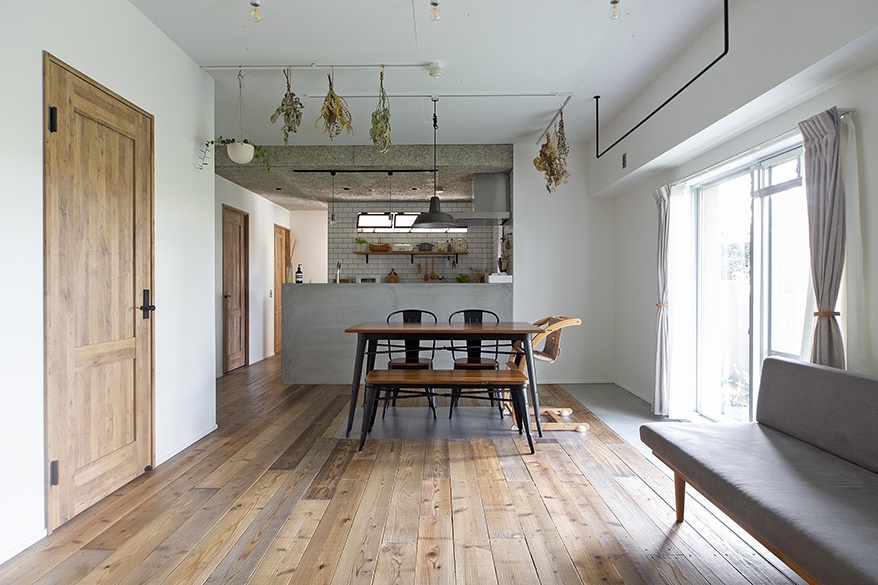 hacorenove style interior, open-plan dining kitchen, rustic oak flooring, concrete counter, white subway tile backsplash, hanging dried herbs, industrial pendant lights, natural daylight, minimalist Japanese renovation aesthetic