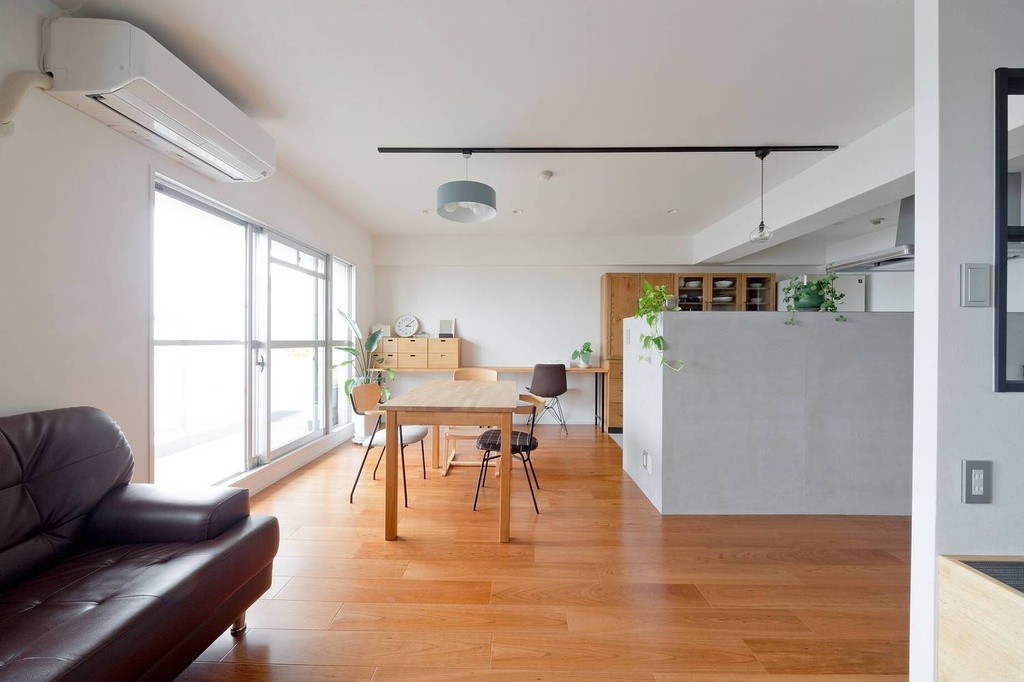 hacorenove style interior, open-plan living dining room, warm oak hardwood floors, concrete kitchen partition, white walls, natural light, indoor plants, minimalist Japanese apartment, pendant lighting, brown leather sofa