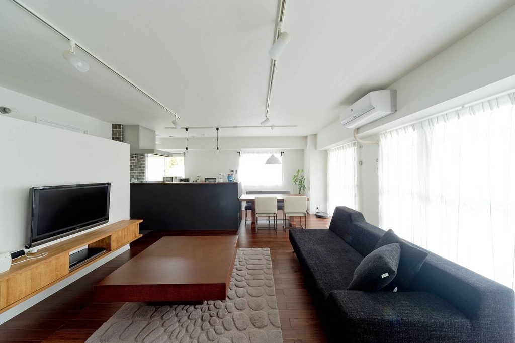hacorenove style interior, open-plan living dining room, dark hardwood floors, white walls and ceiling, dark charcoal sofa, wooden TV console, track lighting, sheer curtains, minimalist Japanese modern atmosphere