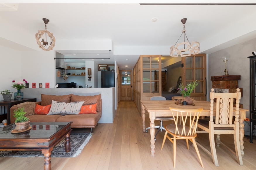 hacorenove style interior, open-plan living dining room, rustic wooden furniture, light oak flooring, carved wooden pendant lights, leather sofa with colorful cushions, glass partition doors, warm eclectic atmosphere