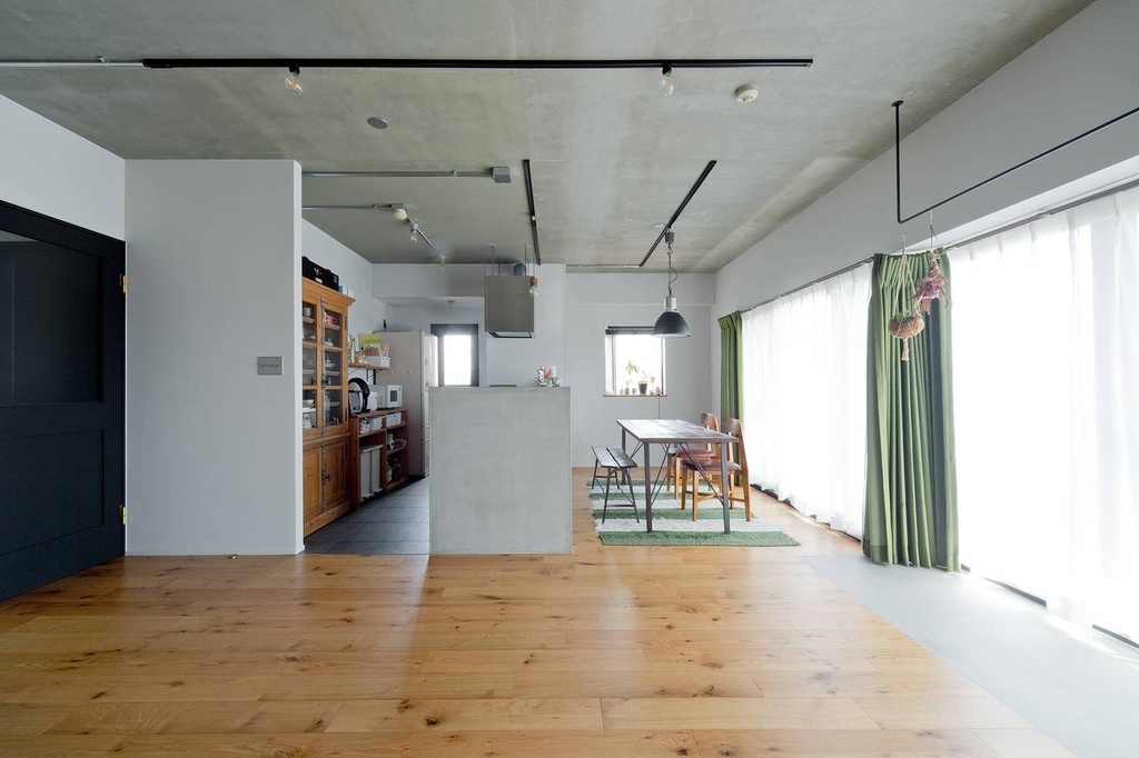 hacorenove style interior, open-plan living dining room, exposed concrete ceiling, natural oak hardwood floors, white walls, black track lighting, green curtains, industrial pendant lamp, minimalist Japanese renovation, bright natural light