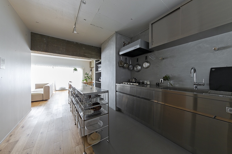 hacorenove style interior, industrial open-plan kitchen, stainless steel counters and cabinets, exposed concrete walls and ceiling, light oak wood flooring, wire storage cart, minimalist Japanese aesthetic, natural daylight, monochromatic grey tones
