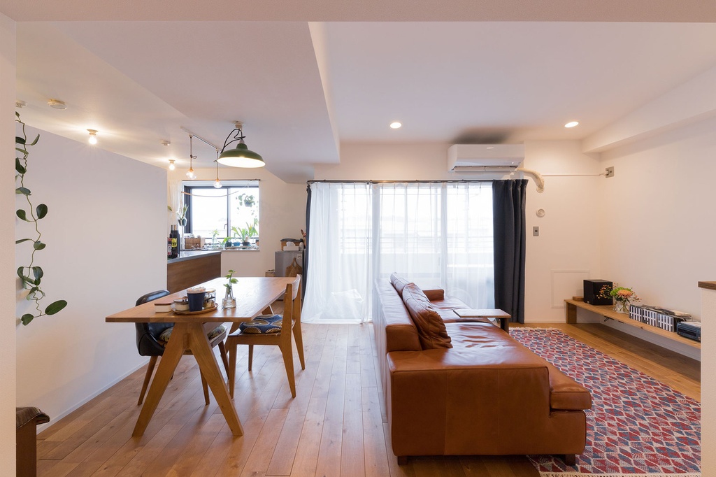 hacorenove style interior, open-plan living dining room, natural oak flooring, tan leather sofa, wooden dining table, white walls, sheer curtains, industrial pendant lights, patterned kilim rug, warm Japanese contemporary atmosphere