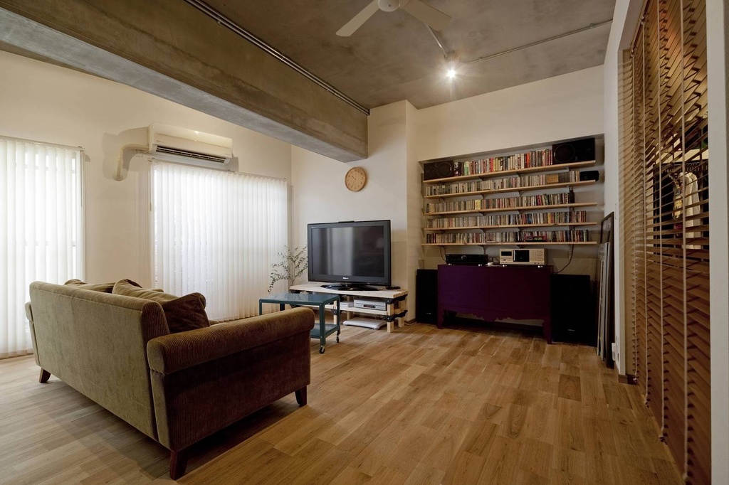 hacorenove style interior, industrial living room, exposed concrete ceiling beam, light oak hardwood floor, white walls, wooden slatted partition, built-in bookshelves, corduroy sofa, ceiling fan, natural daylight, relaxed Japanese loft atmosphere