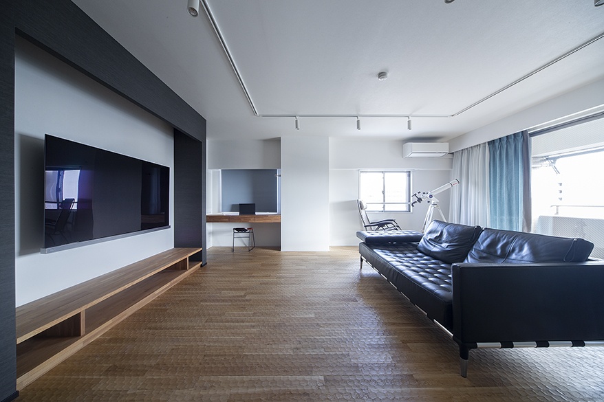 hacorenove style interior, minimalist Japanese living room, dark accent wall with mounted TV, oak parquet flooring, black leather tufted sofa, track lighting, white walls, natural daylight, clean modern aesthetic