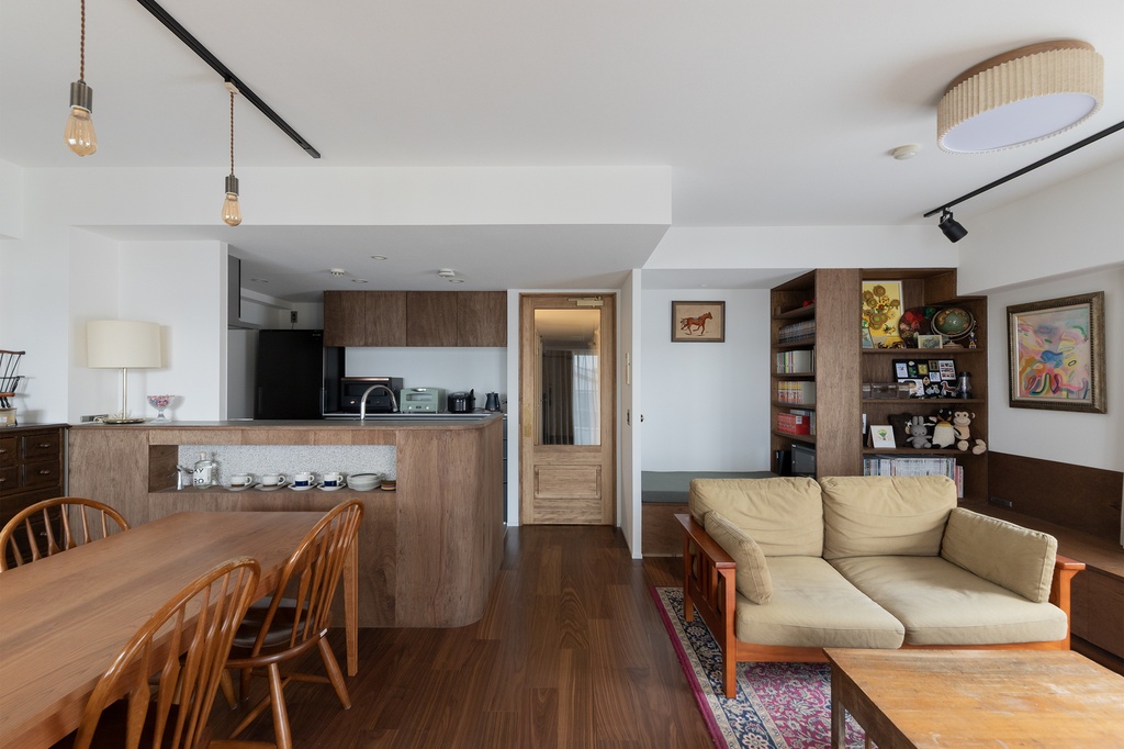 hacorenove style interior, open-plan living dining kitchen, dark walnut flooring, warm wood cabinetry, white walls, Edison pendant lights, beige sofa, built-in bookshelves, Japanese contemporary cozy atmosphere