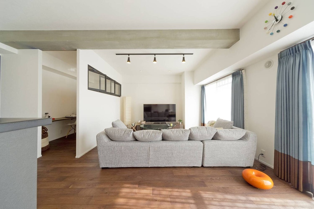 hacorenove style interior, modern Japanese living room, exposed concrete beam, white walls, warm walnut hardwood floor, gray sectional sofa, track lighting, blue curtains, natural light, minimalist open layout