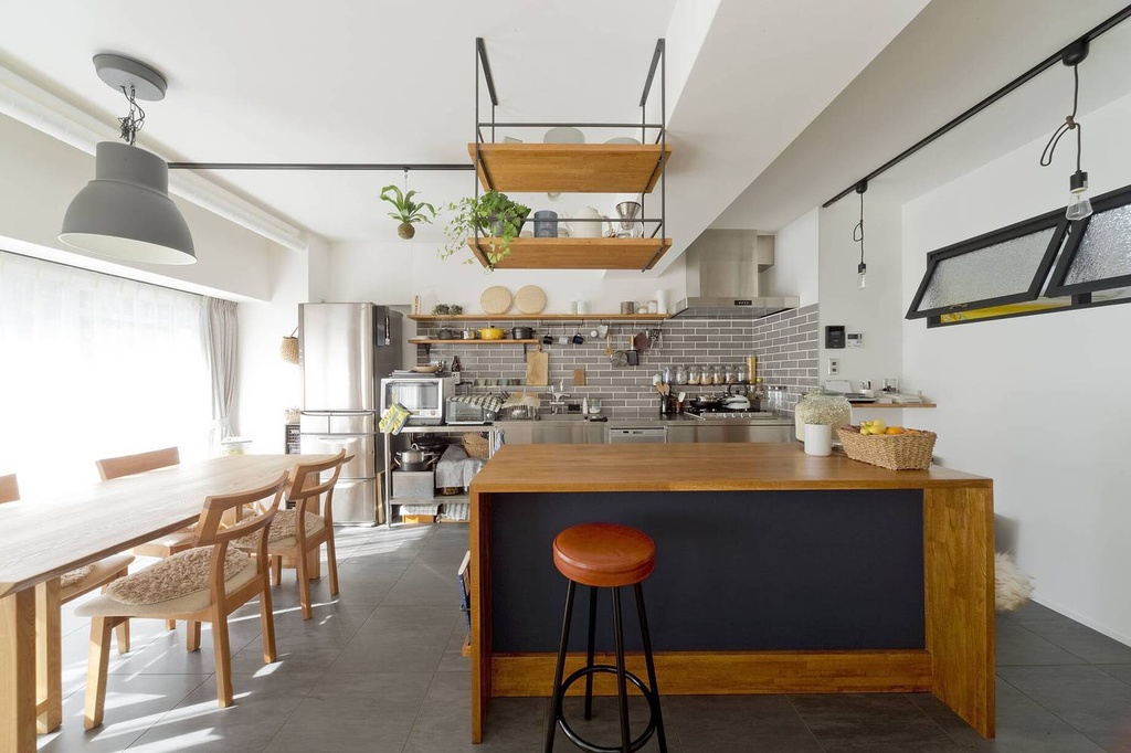 hacorenove style interior, Japanese industrial kitchen-dining, grey subway tile backsplash, wooden island with black panel, suspended open shelving, black metal accents, grey floor tiles, natural light, warm wood tones, lived-in atmosphere