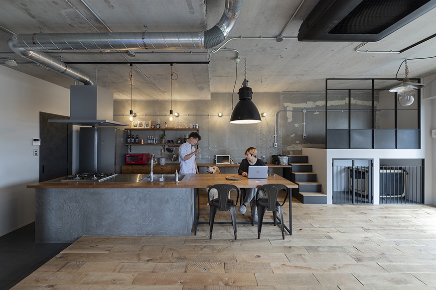 hacorenove style interior, industrial loft kitchen-dining, exposed concrete ceiling, metal ductwork, wood countertop, cement island, rustic oak flooring, black steel-frame partition, warm pendant lighting, raw urban atmosphere