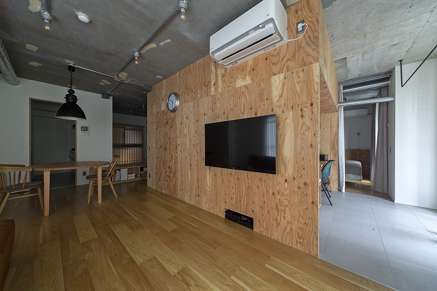 hacorenove style interior, industrial loft living space, plywood feature wall with recessed TV, exposed concrete ceiling, oak hardwood floors, track lighting, black pendant lamp, minimalist Japanese renovation aesthetic