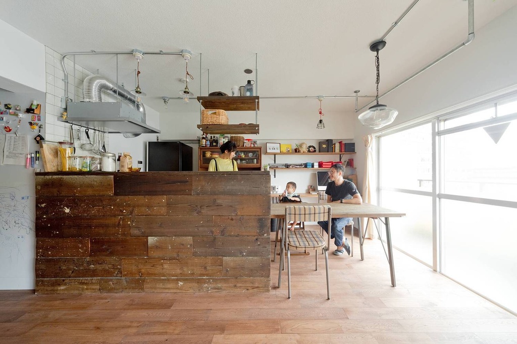 hacorenove style interior, open-plan kitchen-dining room, reclaimed wood counter, exposed metal conduit and ductwork, oak hardwood floors, hanging industrial pendant lights, white walls, natural daylight, Japanese renovated apartment, warm rustic-industrial atmosphere