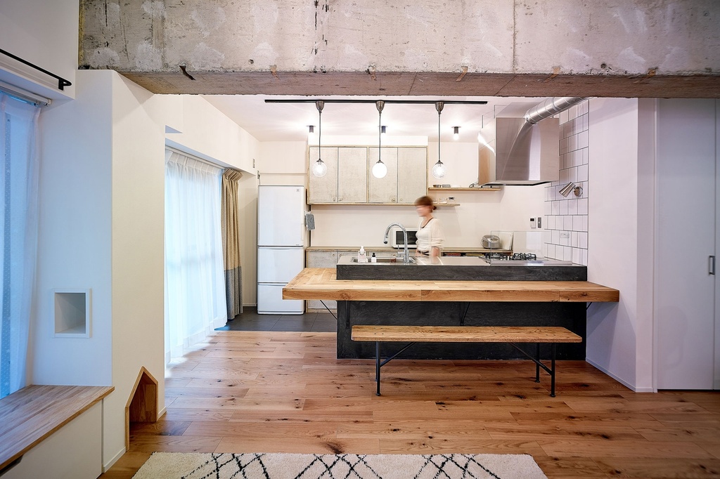 hacorenove style interior, open kitchen with exposed concrete ceiling beams, rustic oak wood flooring, dark island counter with natural wood bar top, white subway tile backsplash, pendant lights, warm industrial atmosphere