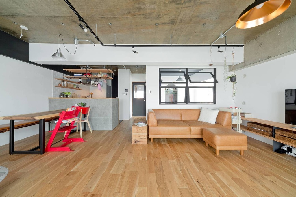 hacorenove style interior, open-plan living dining room, exposed concrete ceiling, light oak hardwood floors, tan leather sectional sofa, black steel track lighting, white walls, industrial-modern Japanese apartment, natural daylight