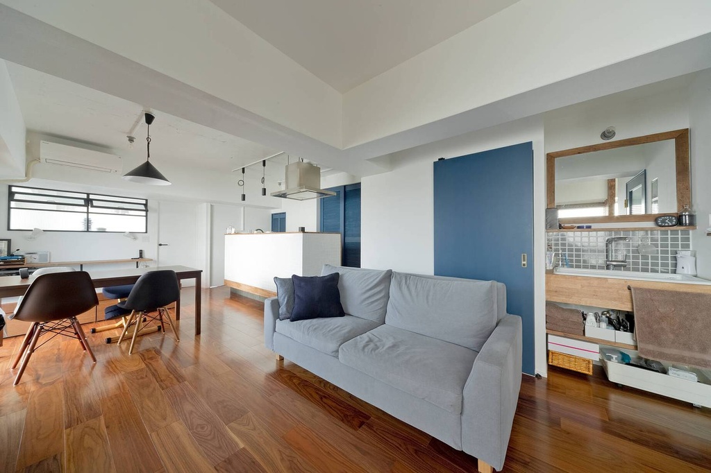 hacorenove style interior, Japanese renovated apartment, open-plan living dining kitchen, warm walnut hardwood floors, white walls, blue accent sliding door, exposed ceiling beams, gray sofa, mid-century chairs, natural daylight, minimal clean atmosphere