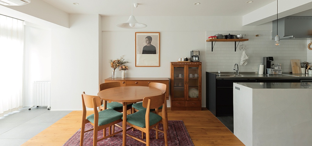 hacorenove style interior, open dining-kitchen, white walls, oak wood flooring, round wooden table, teal upholstered chairs, vintage cabinet, white tile backsplash, pendant light, warm minimalist Japanese aesthetic