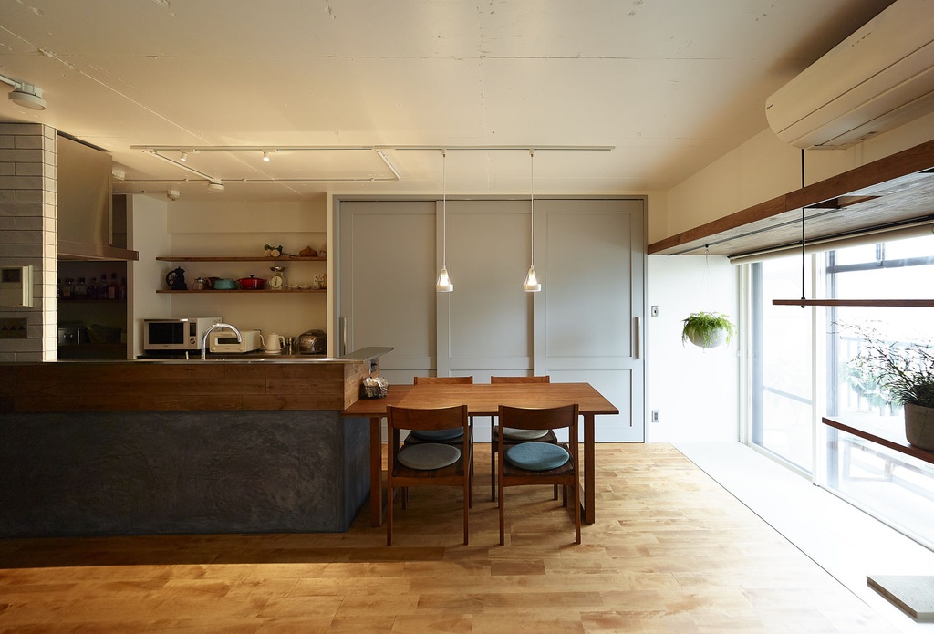 hacorenove style interior, Japanese open-plan kitchen dining room, dark concrete island counter, warm walnut wood dining set, light oak flooring, pendant lights, white walls, exposed beams, natural daylight, minimalist cozy atmosphere