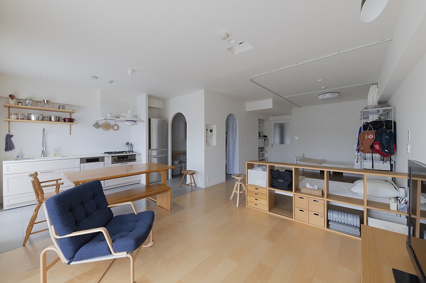 hacorenove style interior, open-plan Japanese apartment, light oak flooring, white walls, arched doorways, wooden shelving room dividers, minimalist kitchen, navy accent chair, natural light, muji-inspired aesthetic