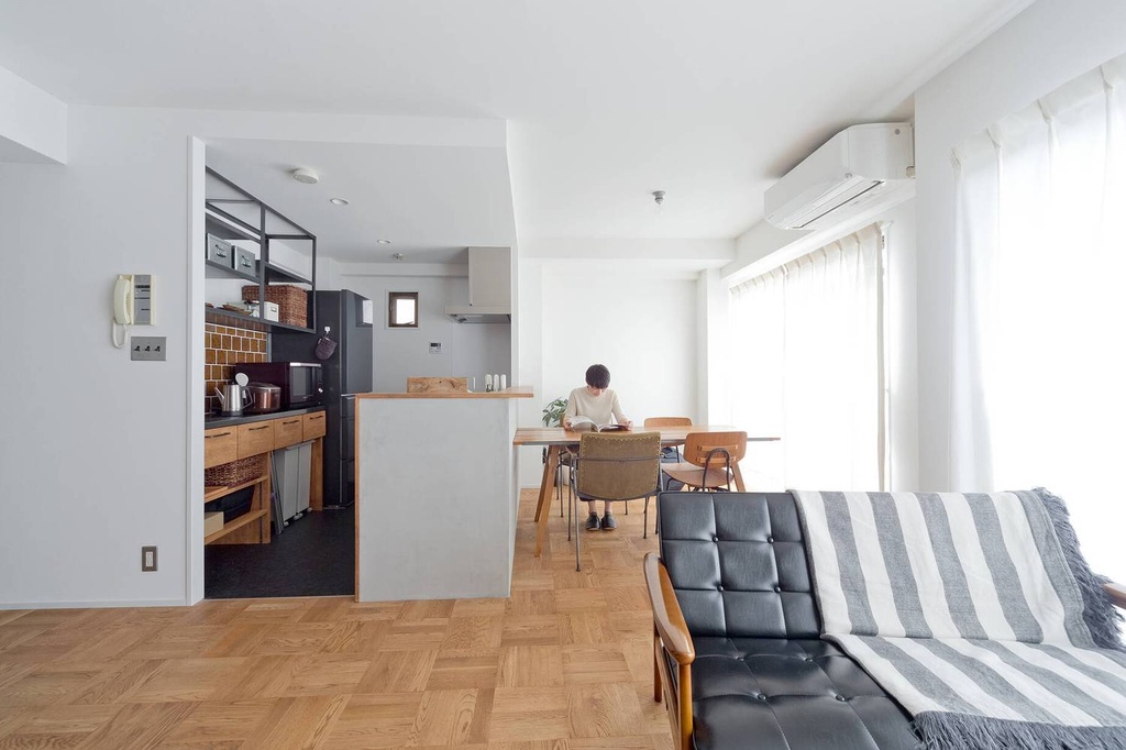 hacorenove style interior, Japanese apartment open-plan living dining kitchen, oak parquet flooring, white walls, black leather sofa, wood counter island, iron open shelving, soft natural light, minimalist warm atmosphere