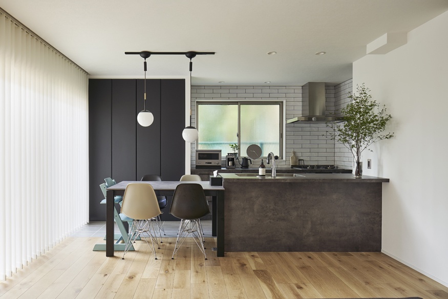 hacorenove style interior, modern Japanese kitchen-dining room, dark concrete island, white subway tile backsplash, light oak flooring, black accent wall, globe pendant lights, sheer vertical blinds, minimalist clean atmosphere