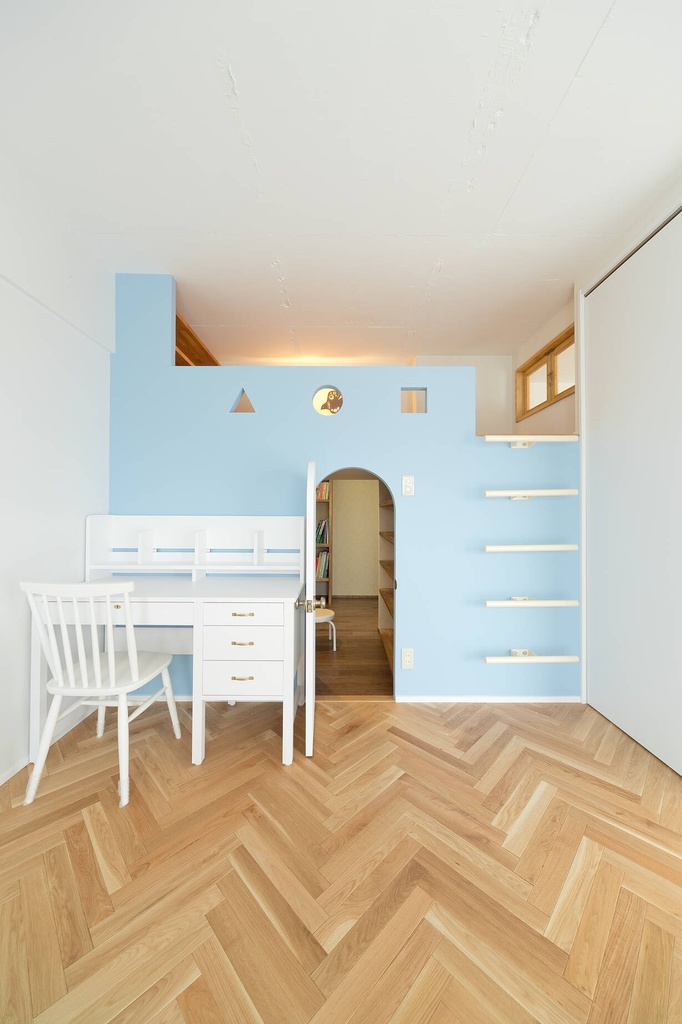 hacorenove style interior, children's room, light blue accent wall with arched doorway, oak herringbone flooring, white desk and chair, loft space, playful geometric cutouts, warm natural light, whimsical Japanese design