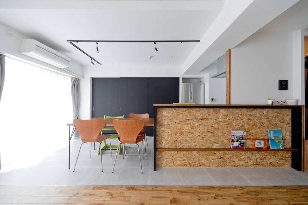 hacorenove style interior, open-plan dining kitchen, OSB panel kitchen counter, natural wood flooring, gray concrete-look tiles, dark accent wall, black track lighting, mid-century wooden chairs, white walls, bright natural light, Japanese modern industrial aesthetic