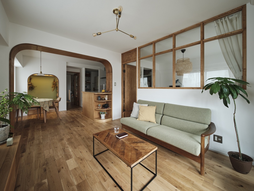 hacorenove style interior, Japanese open-plan living room, warm oak hardwood floors, wooden arch doorway, interior glass partition with wood frames, sage green sofa, brass pendant light, indoor plants, cozy natural atmosphere