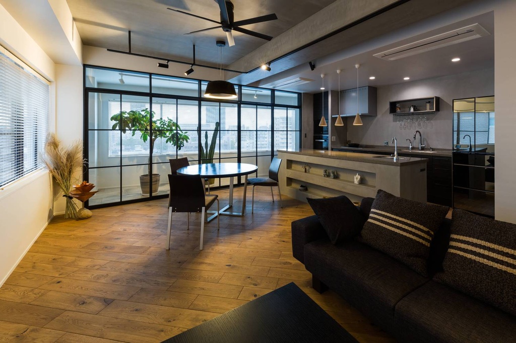 hacorenove style interior, open-plan living dining kitchen, industrial concrete ceiling, black steel-frame glass partition, warm oak hardwood floors, dark sofa, pendant lights, ceiling fan, moody modern atmosphere