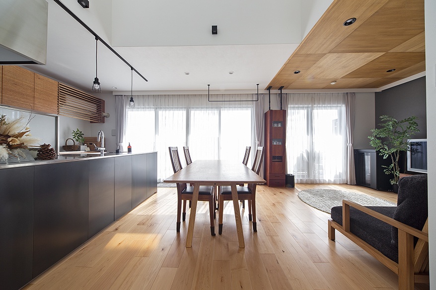 hacorenove style interior, open-plan living dining kitchen, light oak flooring, wooden panel ceiling accent, dark matte kitchen island, black track lighting, sheer curtains, natural daylight, warm Japanese modern atmosphere