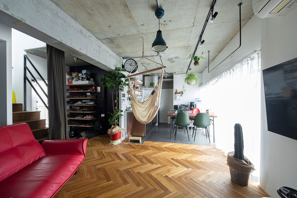 hacorenove style interior, industrial loft living space, exposed concrete ceiling, herringbone wood flooring, red leather sofa, hanging hammock chair, indoor plants, natural light, eclectic bohemian atmosphere